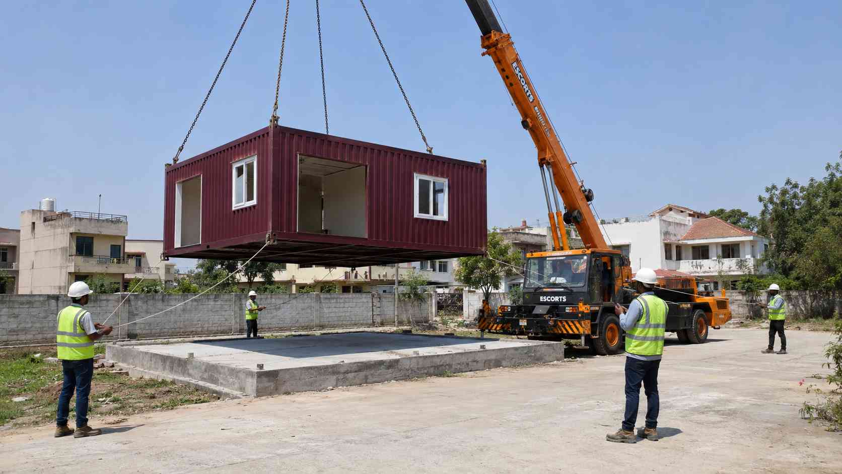 SAMAN affordable container home module being lifted by mobile crane onto a prepared RCC plinth at an Indian residential site — delivery day