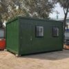 Forest green 20×20 ft SAMAN bunkhouse cabin on a level base at a construction site.