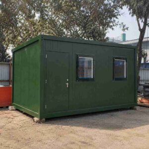 Forest green 20×20 ft SAMAN bunkhouse cabin on a level base at a construction site.