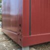 Close-up of burgundy red insulated panel and steel frame joint on a bunkhouse cabin.