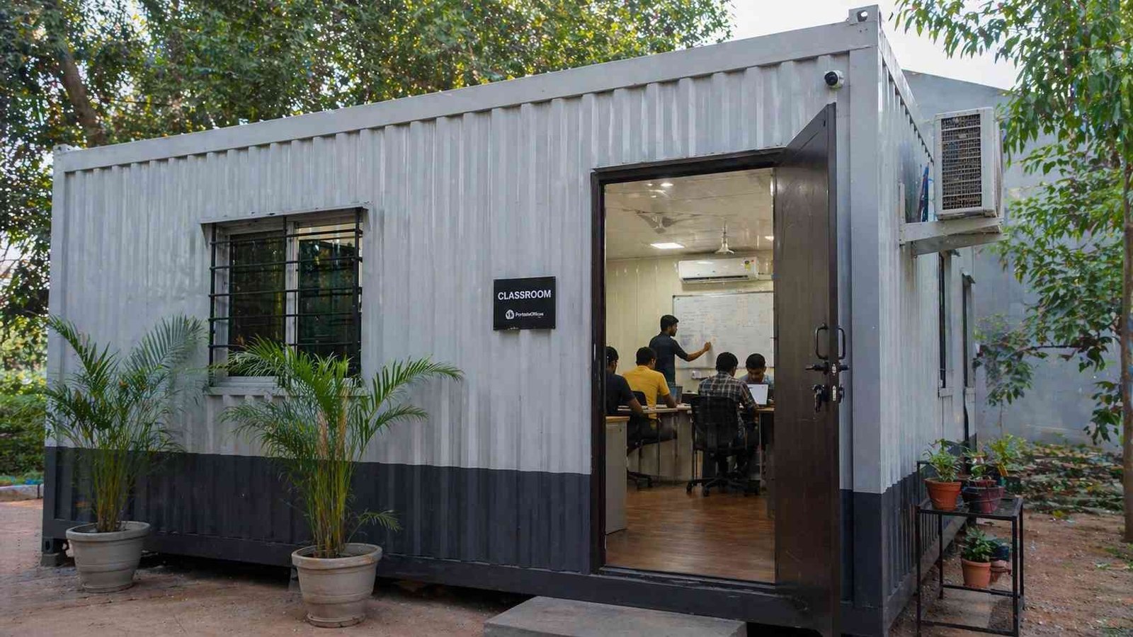 portable office cabin used as classroom with students and whiteboard South India