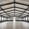 Interior of a commercial shed showing the column-free clear-span steel roof and concrete floor.