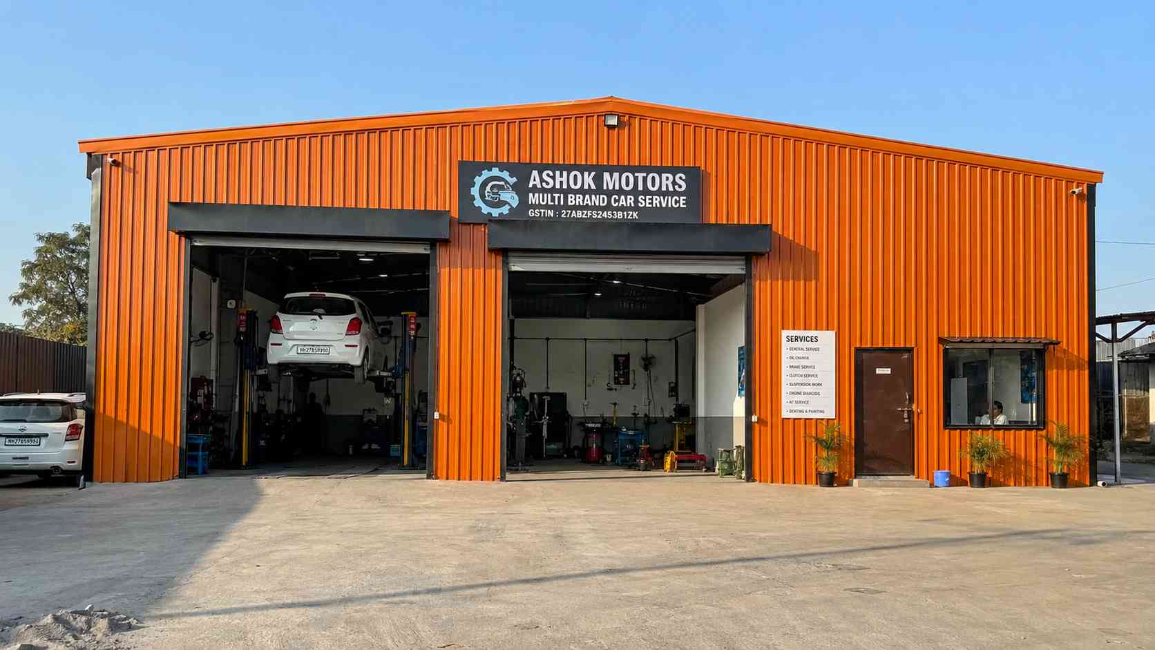 Orange commercial shed used as a vehicle workshop with two open roller-shutter work bays.