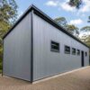 Grey prefabricated building on a gravel plot among trees, in use as a working structure.