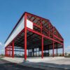 Red structural steel portal frame of a prefabricated building during erection, before cladding.