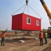 Red portable container office being lifted by crane at an active construction project site in India
