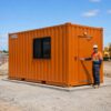 Safety orange container building in use on a worksite with a person beside it for scale.