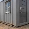 Container office cabin corner detail — corrugated Corten steel texture, ISO corner casting, forklift pocket, steel door, aluminium window with MS grill