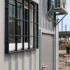 Close-up product detail of a SAMAN container portable office showing MS safety grill, corrugated steel body, and steel entry door fittings