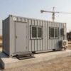 New 20-foot SAMAN container portable office on RCC platform at an Indian construction site with steel door, MS-grill windows, side AC unit, and electrical distribution box