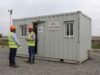 Engineers in PPE walking past a SAMAN container office unit on an active project site.