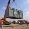 Container office cabin crane placement at Indian construction site — four-point ISO corner lifting, mobile crane, site workers guiding with taglines