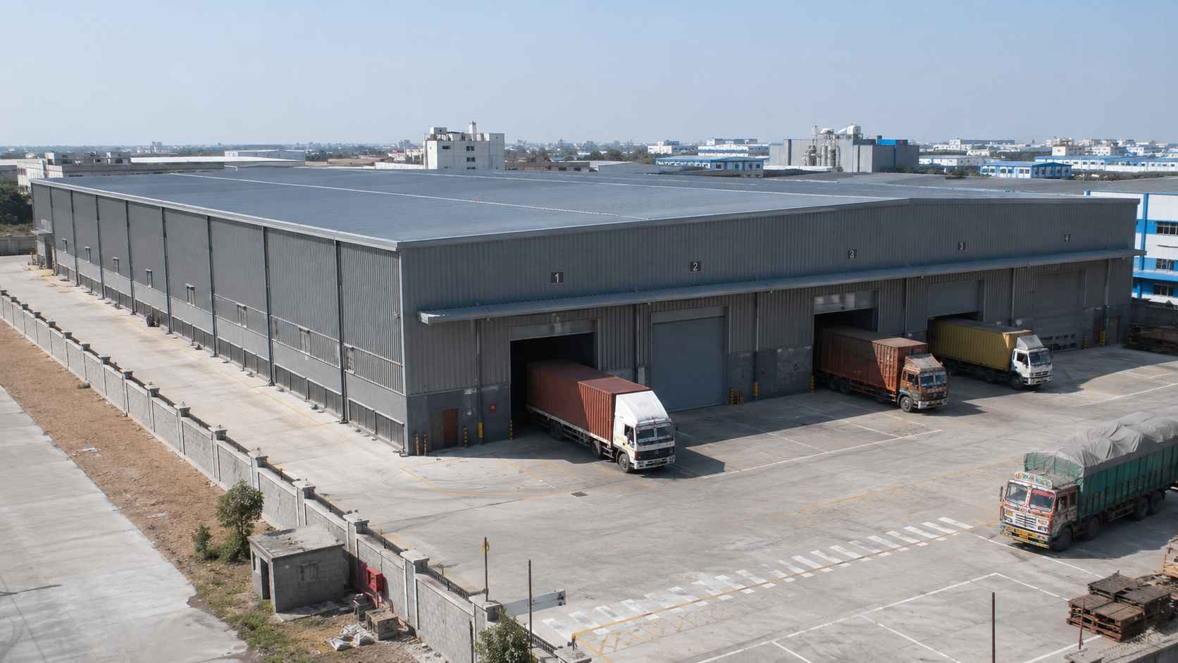 A large custom steel-grey prefabricated warehouse with multiple roller-shutter bays on an industrial estate.