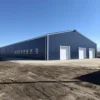 Blue-grey engineered steel building with white roller-shutter doors on a cleared industrial plot