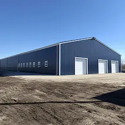 Blue-grey engineered steel building with white roller-shutter doors on a cleared industrial plot