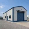 Blue engineered steel structure with a roller-shutter bay on a gravelled industrial plot