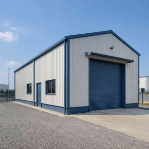Blue engineered steel structure with a roller-shutter bay on a gravelled industrial plot