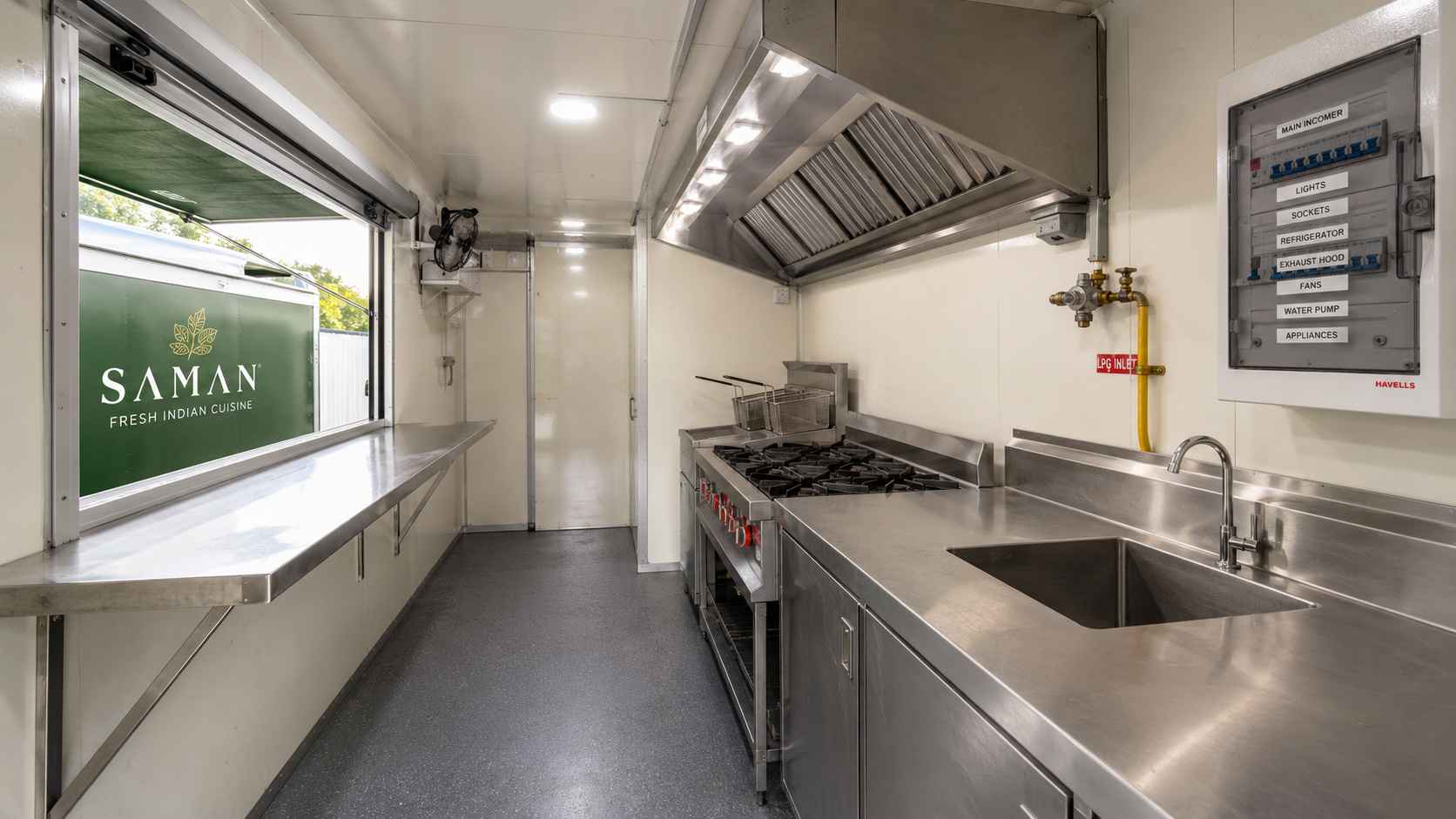 Interior of SAMAN food truck container showing 4-burner LPG range, fryer bay, sink, prep counter, and roll-up service window.