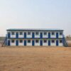 Front view of a SAMAN labor accommodation dormitory block with ground-floor and upper-floor dormitory doors visible.