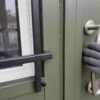 Macro view of a sage green labor camp window grille, door frame and brushed-steel handle in close detail.