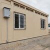 A sandstone beige labor camp side wall with two windows, MS safety grilles and a weatherproof electrical distribution box.