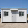 Front view of a SAMAN labor cottage showing MS door with weather hood, two sliding windows with grills, and PUF panel walls
