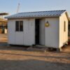 Occupied SAMAN labor cottage on a long-duration project site with workers' boots and hard hat visible near the door