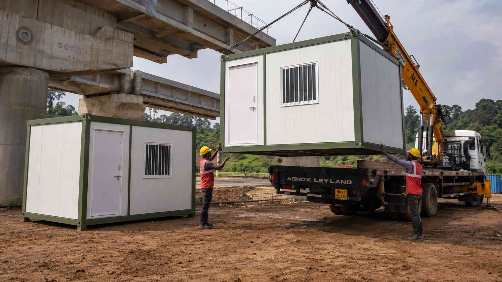 Sage Industrial prefab labor hutment being offloaded from a truck at an Indian bridge construction site by two workers.