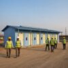 Construction workers with PPE walking out of a SAMAN labor shed at the start of a shift