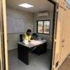 Project supervisor at desk inside a sandstone beige mobile container office reviewing a rigging plan document.