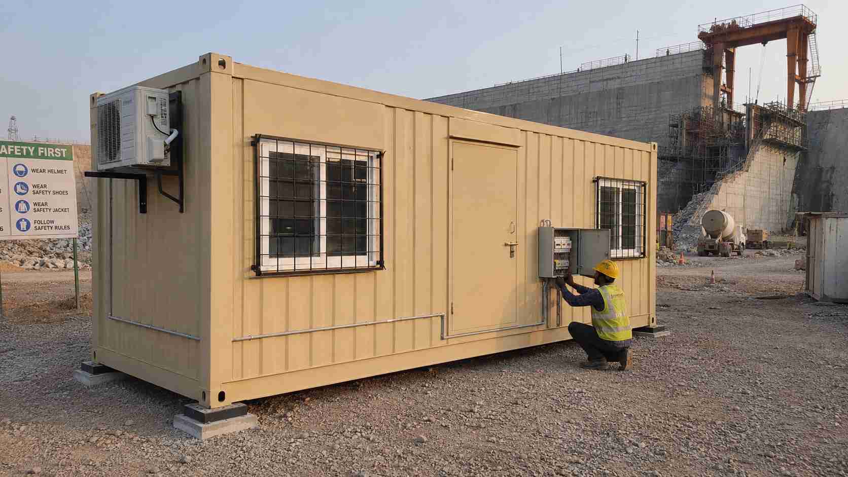 Sandstone beige SAMAN mobile container office during recommission at an Indian dam site, MCB panel being reconnected.