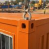 Close-up detail of an ISO corner casting on a safety orange mobile container office with sling hook engaged.