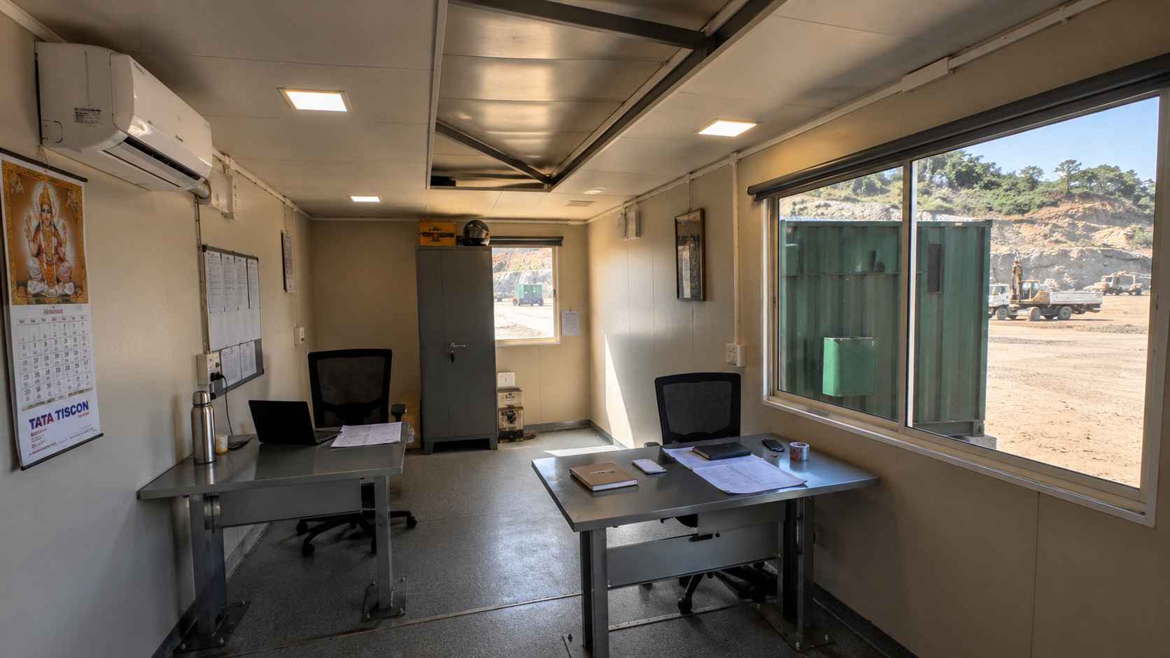 Interior of a forest green mobile container office showing anchored desks, detachable AC, and welded roof brace above.