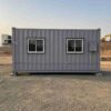 Steel grey mobile container office in side profile at an empty levelling pad with a work front in the distance.