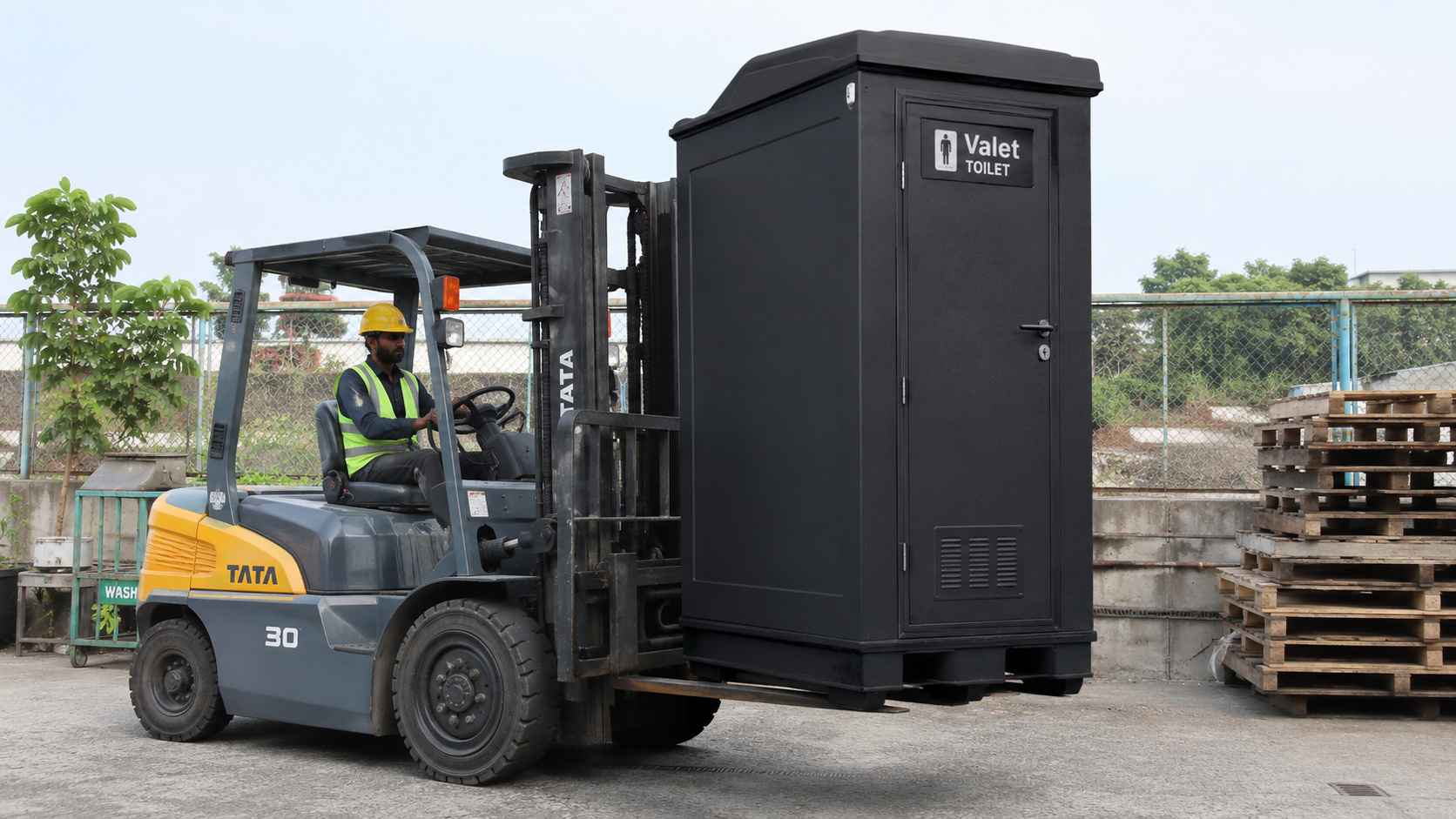 Black mobile toilet carried by a forklift into position at an industrial yard