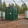 Forest green mobile toilet at a remote wooded work site with cranes behind