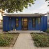 Front entrance of a royal cobalt blue modern container home with covered porch and glazed door.