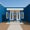 Covered entrance of a blue modern container home with glass pergola roof and framed windows.