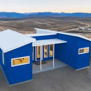 Royal cobalt blue modern container home with white butterfly roof on an open hillside plot at dusk.