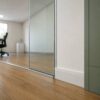 Close-up of the frameless glass partition meeting the wood-look vinyl flooring inside the modern office cabin