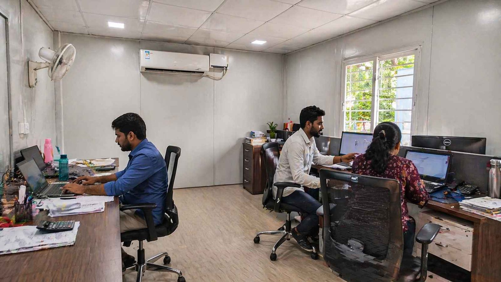 Portable cabin interior used as office workspace with three people working AC false ceiling and natural light