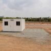 Pure White modular container office front-angle view with prepared pad grid extending beside it for future Unit 2 placement.