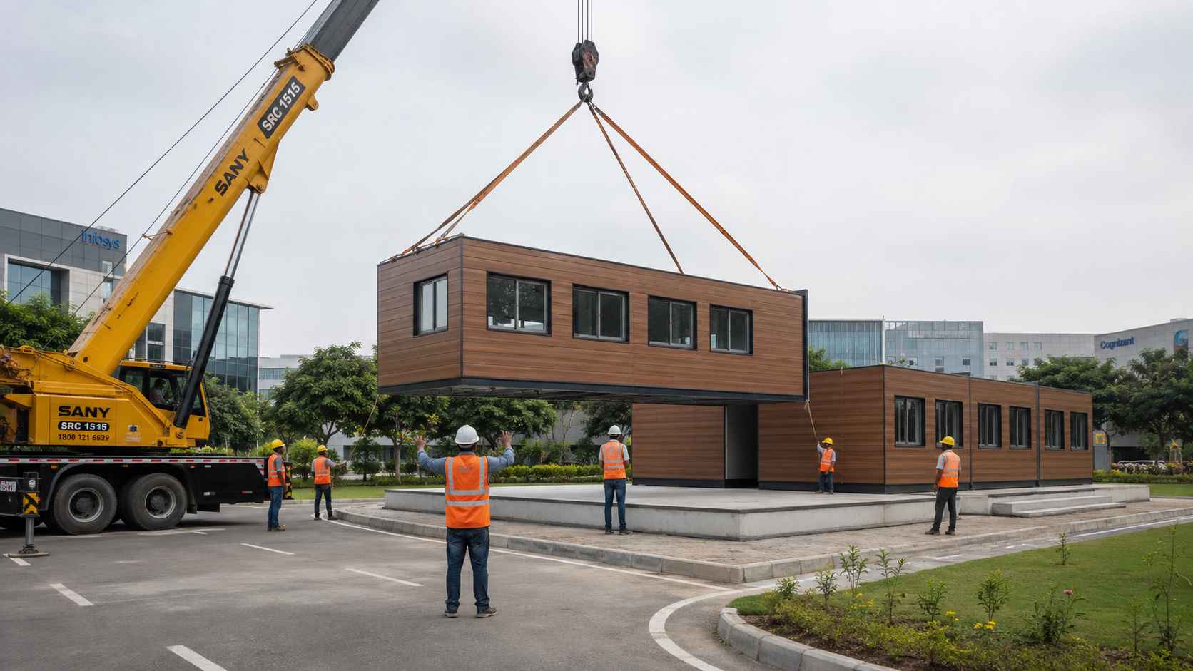 A 15-ton mobile crane placing a modular office cabin structural section onto an RCC plinth, with three previously placed sections joined alongside.
