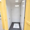 Inside a movable toilet cabin showing a clean squat pan, water inlet and wall vent