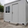 Pearl Grey office cabin front-angle view, lockable steel door, concrete foundation pad and door threshold step.