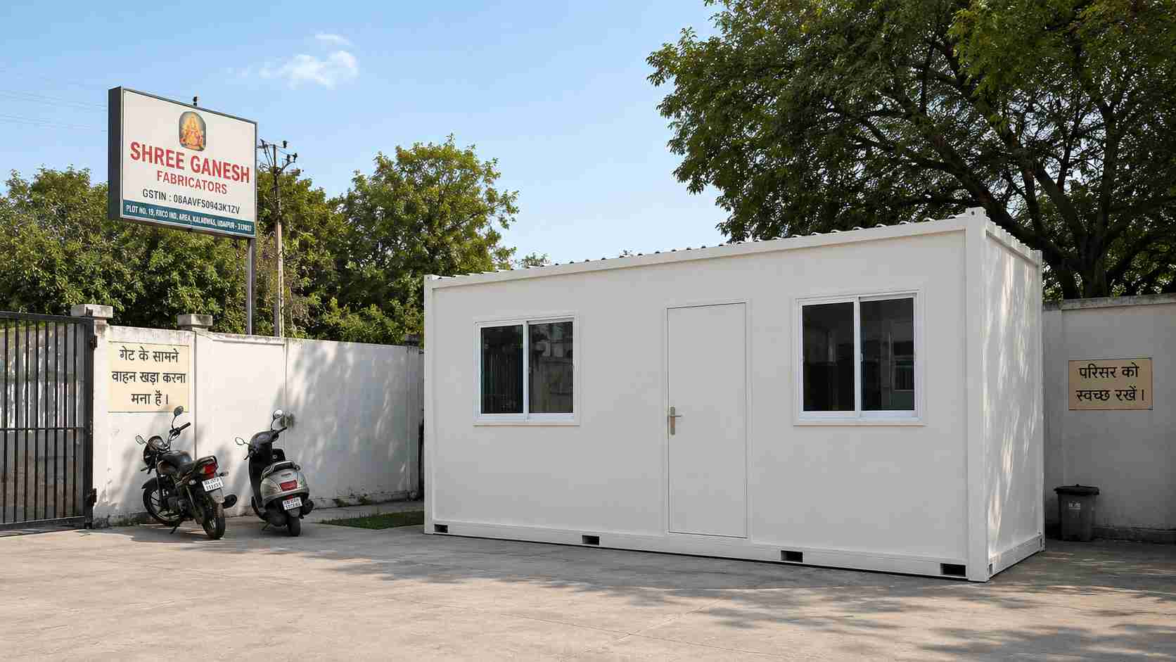 White office cabin installed inside an Indian SME compound, concrete pad, perimeter wall and gate visible.