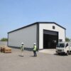Off-white PEB steel building in use at an Indian industrial compound with workers in safety gear nearby