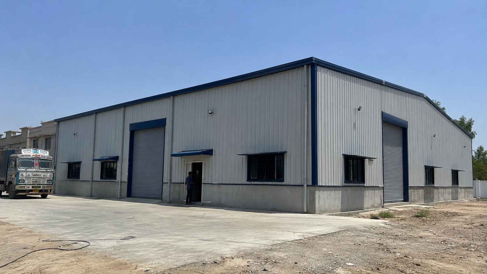 Completed 120×30 ft navy-trimmed PEB steel structure with a truck and worker for scale.