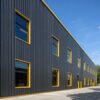 Close view of charcoal ribbed steel cladding with yellow-framed windows on a PEB steel structure.