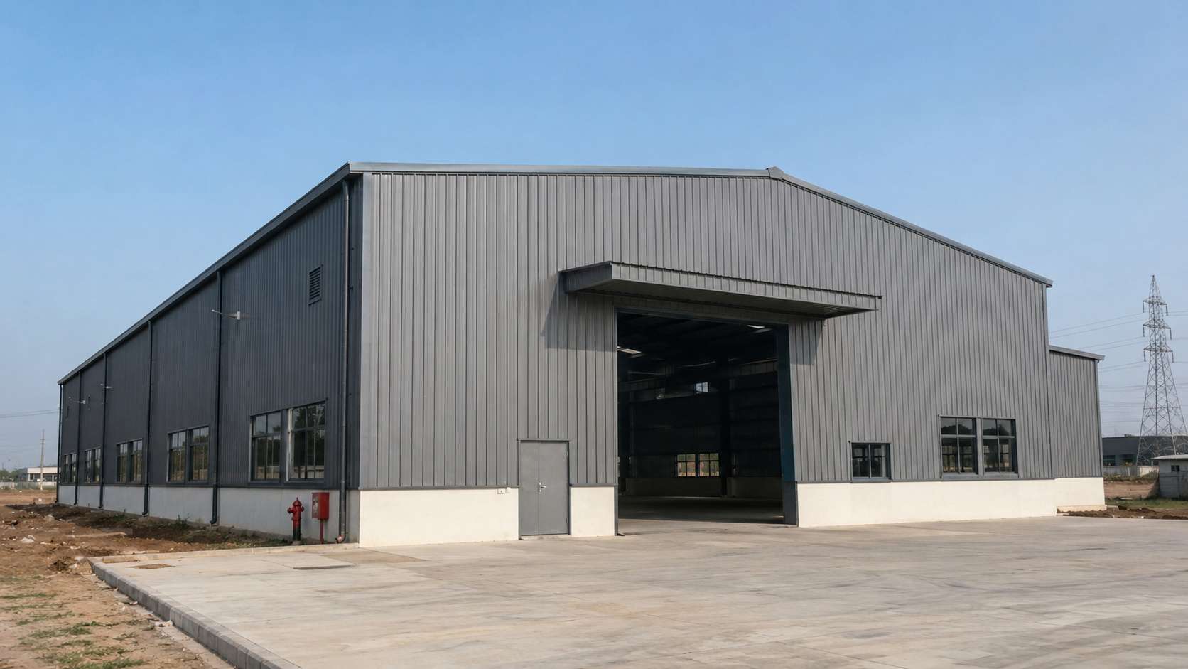 A completed steel-grey PEB steel structure on an Indian industrial plot under clear sky.